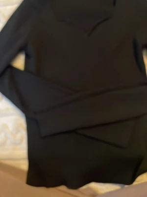 Svart långärmad topp med v-ringning från STOCKHOLM LM STUDIO  - En stilren svart långärmad topp med v-ringning från STOCKHOLM LM STUDIO Tröjan har en figurnära passform och är tillverkad i ett mjukt, stretchigt material som sitter snyggt på kroppen. Perfekt basplagg för alla tillfällen.