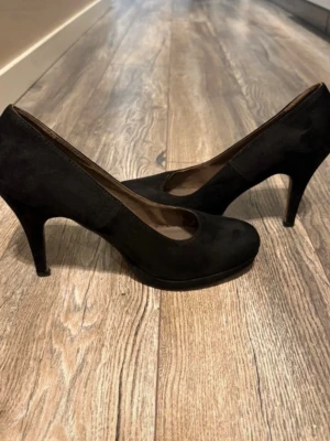 Svarta pumps från Tamaris - Stilrena svarta pumps från Tamaris i mockaimitation med klassisk rund tå och smal klack. Insidan är fodrad med mjukt material för extra komfort. Perfekta för dig som vill ha en tidlös och elegant sko till garderoben. Används några gånger men inte skadade
