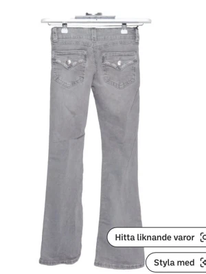 Grå bootcut jeans med fickdetaljer - Snygga grå bootcut jeans med dekorativa bakfickor och silvriga knappar. Jeansen har en klassisk femficksmodell och lätt utsvängda ben. Perfekta för dig som gillar en avslappnad men trendig look.