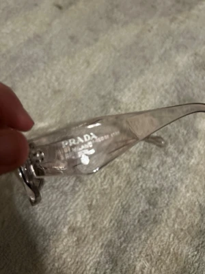 Transparenta solglasögon från Prada - Snygga solglasögon från Prada med transparent båge och rektangulär form. Glasögonen har en modern och stilren look med diskret logga på sidan. Perfekta för dig som vill ha en clean och trendig accessoar. 