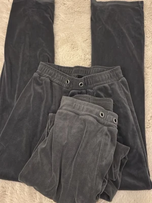 Gråa mjukisbyxor i velour 2st - Mysiga gråa mjukisbyxor i mjuk velour med resår och dragsko i midjan. Byxorna har raka ben och metallöljetter framtill för snöre. Perfekta för chill eller hemmadagar.