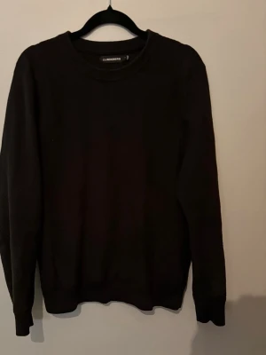 J.Lindeberg tröja  - En stilren svart tröja från J.Lindeberg med rund halsringning och diskret struktur i materialet. Tröjan har långa ärmar och ribbade muddar vid ärmslut och nederkant. Perfekt för en clean och enkel look.
