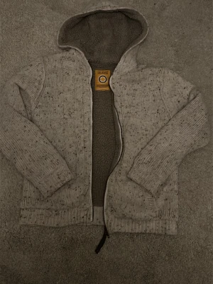 Cardigan - Mysig ljusgrå stickad hoodie från Blend med dragkedja och huva. Utsidan är melerad och insidan är fodrad med mjuk teddy för extra värme. Perfekt för kyliga dagar och har ribbade muddar vid ärmslut och nederkant. Passar bra för både tjej och kille.