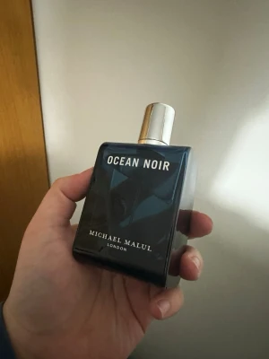 Ocean Noir parfym Michael Malul - Ocean Noir från Michael Malul är en elegant parfym i en mörkblå, fyrkantig glasflaska med silverfärgad spraykork. Flaskan har en stilren design med tydlig logga och text framtill. Perfekt för dig som gillar exklusiva dofter med modern känsla. 90% kvar! Obs! Saknar original förpackning