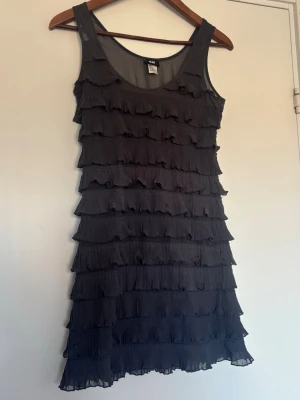 Svart volangklänning från H&M - Supersöt svart klänning från H&M med flera lager volanger. Ärmlös modell med rund halsringning 