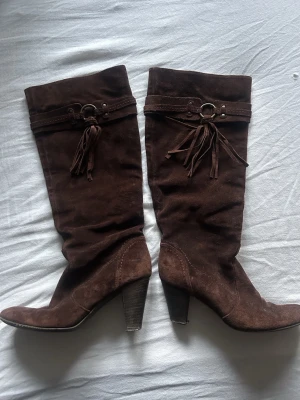 Bruna mockastövlar med klack och fransar - Snygga bruna stövlar i mocka med hög/mellan klack och dekorativa fransar samt ringdetalj upptill. Skorna är jätte snygga och sköna att ha på sig, köpte dom när jag var i Italien för några år sedan. Storlek 35 står det men skulle mer säga att det är 37. Skulle säga att det är fina i skicket men man ser att dom är använda. Skriv för mer frågor, priset går att diskutera💕