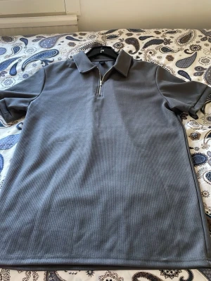 Grå ribbad polotopp med dragkedja - Snygg grå ribbad polotopp med kort ärm och halv dragkedja framtill. Klassisk krage och relaxed fit, perfekt till jeans eller kjol. Materialet känns mjukt och bekvämt mot huden.