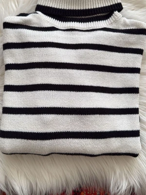 Randig stickad tröja från Pieces - Snygg stickad tröja från Pieces i vitt med svarta horisontella ränder och ribbad polokrage. Perfekt för dig som gillar klassisk och stilren look. Tröjan är mjuk och skön, passar till många outfits.