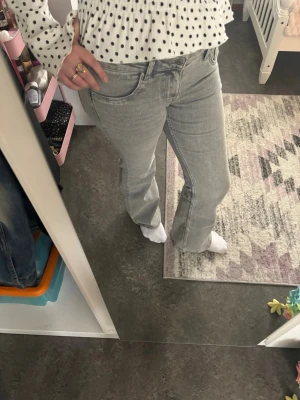 Ljusgrå lågmidjade utsvängda  jeans - Säljer ett par ljusblå jeans med utsvängd passform och klassisk femficksdesign. Jeansen har låg midja och stängs med knapp och dragkedja. Perfekta till en avslappnad och trendig look. Materialet är denim i bomull.