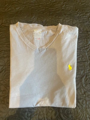 Grå v-ringad t-shirt från Polo Ralph Lauren - Snygg grå t-shirt från Polo Ralph Lauren med v-ringning och klassisk gul broderad logga på bröstet. Tillverkad i mjuk bomull som känns skön mot huden. Perfekt basplagg med clean look och normal passform. Postad dagen eller dagen efter köpet.