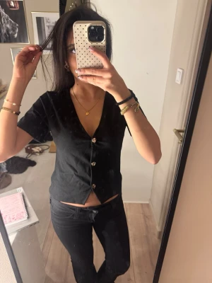 Svart croppad topp med knappar - Säljer en svart croppad topp med v-ringning och korta ärmar. Toppen har dekorativa knappar framtill och är enkel men snygg att matcha med jeans eller kjol. Perfekt för dig som gillar en stilren look.