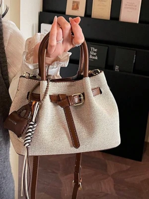 Beige handväska med bruna detaljer - Snygg beige handväska i canvas med bruna läderdetaljer och dekorativt bälte framtill. Väskan har både handtag och axelrem samt en liten charm i läder och snöre. Perfekt storlek för det viktigaste och stängs med magnetknapp.