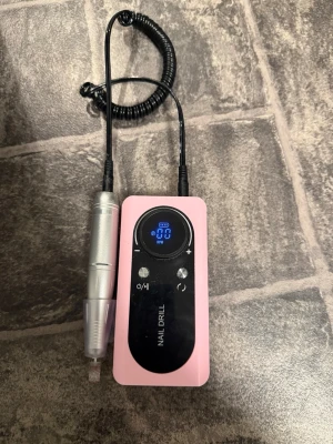 Elektrisk nagelfil rosa med display - Elektrisk nagelfil i rosa med digital display och silverfärgad handdel. Perfekt för att fila, forma och polera naglar. Utrustad med justerbar hastighet och tydliga knappar. Kompakt och smidig design för enkel användning hemma.