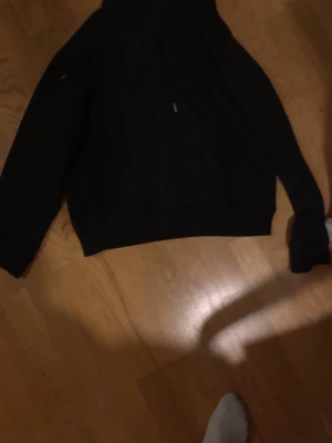 Svart hoodie med huva och dragsko - Säljer en klassisk svart hoodie med huva och dragsko. Hoodien har en avslappnad passform och ribbade muddar vid ärmslut och nederkant. Perfekt för dig som gillar en enkel och stilren look. Materialet känns mjukt och bekvämt.