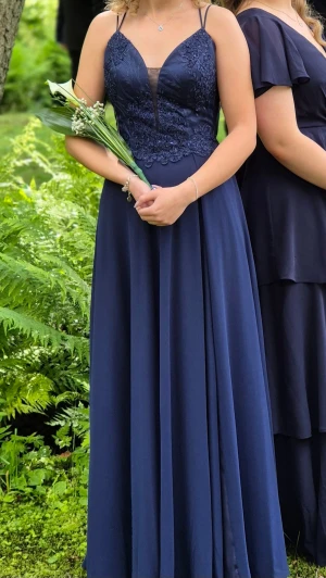 Marinblå balklänning med spetsdetaljer - Elegant marinblå långklänning med smala axelband, spetsdetaljer på livet och v-ringning framtill. Klänningen har snörning i ryggen som gör att den passar många. Endast använd en gång. Passar mig som är xs-167cm lång, hade en liten klack på mig. Perfekt balklänning! Nypris 3200kr. Fler bilder kan fixas!
