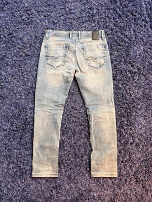 Diesel jeans - Säljer ett par jeans från Diesel med klassisk femficksdesign och diskreta slitningar. Jeansen har en rak men också smal passform och är tillverkade i mjuk denim med stretch. Perfekta för en avslappnad och trendig look. De sitter kortare än L34 ca L31. Färgen och passformen är otrolig därav priset, hör av er vid minsta fundering!