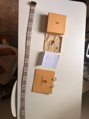 Burberry vändbart bälte med monogram - Säljer ett vändbart bälte från Burberry med klassiskt beige rutmönster på ena sidan och svart läder på andra. Bältet har ett guldfärgat BB-monogram som spänne och kommer med originalpåse, box och påse. Perfekt accessoar för att lyfta din outfit.
