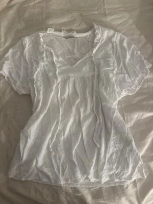 Vit blus med knyt och volang - Söt vit blus i ett tunt material med korta ärmar. 