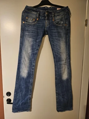 Blå jeans Herrlicher - Säljer ett par blå bootcut jeans från Herrlicher med snygga slitningar och tvättade detaljer. Jeansen har fem fickor, låg midja och klassisk knappgylf. Materialet är denim i bomull och passformen är rak. Väldigt låga i midjan.