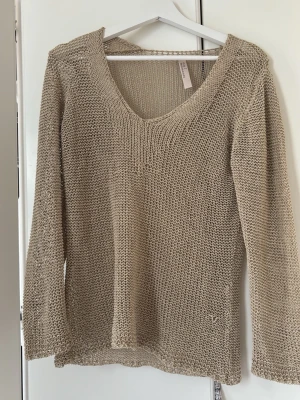 Beige stickad tröja med v-ringning - Säljer en beige stickad tröja med v-ringad hals och långa ärmar. Tröjan har en lös passform och är stickad i ett grovt garn som ger en avslappnad look. Perfekt att slänga på sig över ett linne eller t-shirt.
