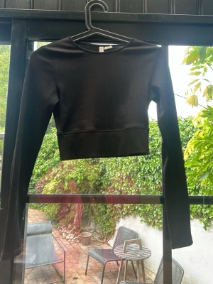 Svart ribbad croppad topp H&M Divided - Svart långärmad topp från H&M Divided. Modellen är croppad och har en ribbad struktur som ger en snygg och trendig look. Träningströja kortare i magen