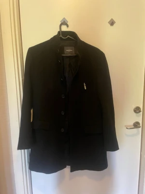 Svart klassisk rock  - Stilren svart rock med knäppning framtill och två fickor med lock. Rocken har en rak passform och är helfodrad, perfekt för en snygg och tidlös look. Passar utmärkt till både jeans och kostym.