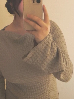 Beige tröja med vida ärmar - Säljer en beige långärmad tröja med bred båturringning och vida ärmar. Tröjan har ett strukturerat, våfflat mönster och är tillverkad i ett mjukt stickat material. Perfekt för dig som gillar avslappnad och trendig stil.