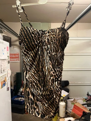 Oanvänd Baddräkt med leopardmönster - Säljer en oanvänd snygg baddräkt med leopardmönster i brunt, svart och beige. Modellen har tunna axelband och rynkade detaljer längs sidorna för en cool look. Materialet är stretchigt och följsamt, perfekt för strand eller poolhäng. Alla lappar sitter kvar även hygiene lappen i grenen sitter kvar då den är oanvänd. Nypriset är 849kr. 