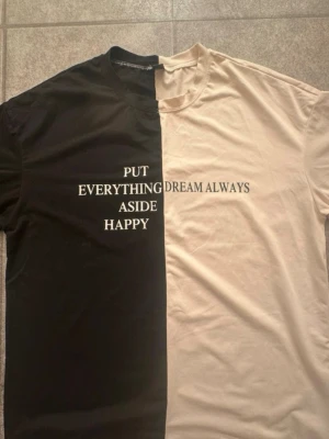 Ny. Tvåfärgad t-shirt med text - Unik t-shirt i svart och beige med tydlig mittsöm. Framsidan har tryckt text: 'PUT EVERYTHING ASIDE HAPPY DREAM ALWAYS'. Klassisk rund hals och korta ärmar. Tillverkad i mjuk bomull för skön känsla och avslappnad passform. Storlek xs, men mycket oversize och kan passa större storlekar. Bröst 114cm, längd 70cm.