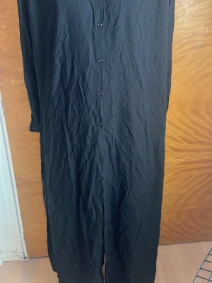 Svart lång skjortklänning med knappar, Art dress. - En svart långklänning med knäppning hela vägen fram och baktill. Den har även slits på båda sidorna och fram och bak då man ska kunna knäppa den hur långt man vill! Mycket bra skick (nästan som ny) och köptes för ungefär 2000kr.
