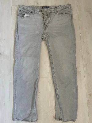 Ljusgrå raka jeans - Säljer ett par ljusgrå jeans med rak passform och klassisk femficksdesign. Jeansen har normal midja och är tillverkade i denim. Perfekta för en avslappnad och stilren look.
