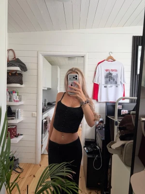 Svart croppad korsett-topp - Snygg svart korsett-topp med smala axelband och croppad passform. Toppen har snörningsdetaljer framtill och är perfekt för att skapa en edgy look. Materialet känns lätt och passar bra till både jeans och kjol.