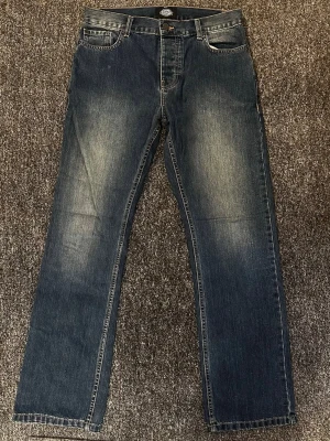 Blå raka jeans från Dickies - Klassiska blå jeans från Dickies med rak passform och snyggt slitna detaljer framtill. Jeansen har fem fickor, normal midja och kontrastsömmar. Tillverkade i slitstark denim som passar perfekt till en avslappnad stil.