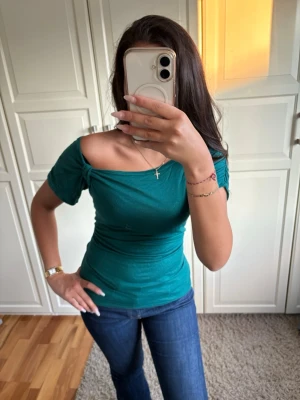 Grön offshoulder topp - Snygg grön offshoulder topp med korta ärmar och figurnära passform. Perfekt till jeans eller kjol för en trendig look. Materialet känns mjukt och stretchigt, vilket gör den bekväm att bära hela dagen.