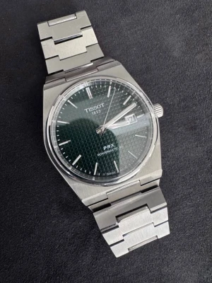 Tissot PRX Powermatic 80 klocka - Snygg Tissot PRX Powermatic 80 med grön urtavla och datumvisning. Klockan har ett stilrent armband i rostfritt stål och en modern, kantig design. Perfekt accessoar för dig som gillar klassisk men trendig stil.