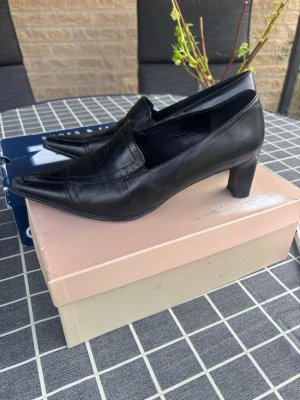 Svarta spetsiga pumps i skinn - Snygga svarta pumps med spetsig tå och låg klack. Skorna är tillverkade i slätt skinn och har en klassisk, stilren design utan synligt märke. Perfekta för dig som gillar en elegant och tidlös look.