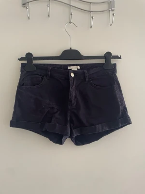 Mörkblå denimshorts med uppvik - Snygga mörkblå shorts i denim med klassisk femficksmodell och uppvikta benslut. De har knapp- och dragkedjestängning samt bälteshällor i midjan. Perfekta för en avslappnad och trendig look.  Dom är även lågmidjade.