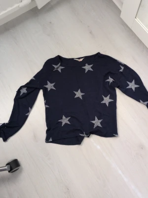 Mörkblå tröja med stjärnor H&M - Mysig mörkblå tröja från H&M med silverfärgade stjärnor över hela plagget. Tröjan har rund halsringning och långa ärmar. Perfekt för dig som gillar en avslappnad och trendig stil.