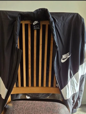 Svart och vit Nike jacka. Storlek M - Nike jacka i svart med breda vita paneler och stor Nike-logga på ryggen. Jackan är I mycket gott skick så gott som ny. 
