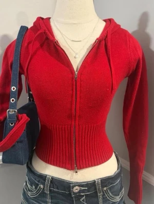 Röd croppad stickad hoodie - Trendig röd stickad hoodie med dragkedja framtill och ribbad midja. Croppad modell med långa ärmar och huva med dragsko. Perfekt för en cool och avslappnad stil.priset går att diskuteras vid en snabb äffar😊