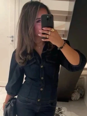 Zara jeanstopp - Snygg mörkblå jeansblus med markerad midja och trekvartsärmar. Blusen har framfickor och stängs med silverfärgade knappar framtill. Perfekt till både jeans och kjol för en trendig look.