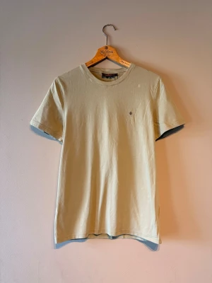 Grön Morris t-shirt  - Snygg beige t-shirt i bomull med korta ärmar och rund hals. På bröstet finns en liten broderad detalj som ger en stilren touch. Perfekt basplagg för en avslappnad look.