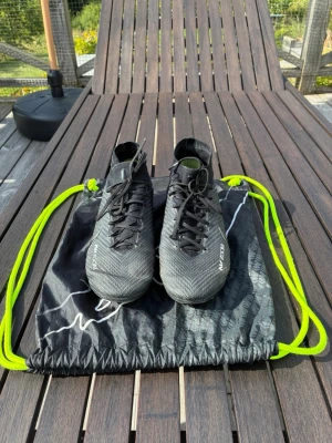 Svarta Nike Mercurial fotbollsskor - Säljer ett par svarta Nike Mercurial fotbollsskor med högt skaft och snörning. Skorna har en modern design med diskreta vita detaljer och är tillverkade i ett lätt syntetmaterial. Perfekta för dig som vill ha bra grepp och kontroll på planen.