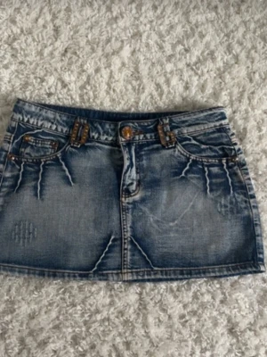 Blå jeanskjol i minilängd - Snygg blå jeanskjol i minilängd med slitna detaljer och dekorativa sömmar. Säljer den då den tyvärr inte passar mig. Skicka för mått och fler bilder!