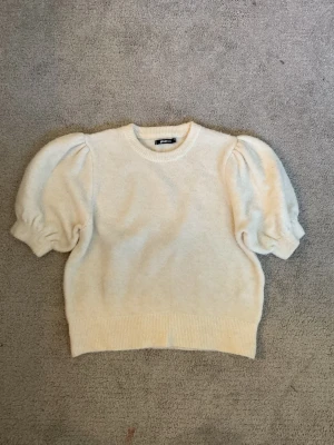 Puffärm tröja från Gina tricot - Supersöt krämvit tröja med puffärmar och rund hals. Tröjan har ribbade muddar vid ärmslut och nederkant, och är gjord i ett mjukt, stickat material. Perfekt för dig som vill ha en trendig och cozy look.