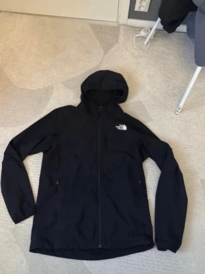 Svart vindjacka från The North Face - Snygg svart vindjacka från The North Face med huva. Bekväm till sena sommardagar eller småkyliga dagar. Använd fåtals har endast ett rivmärke som ni ser på bilden men inget som syns 