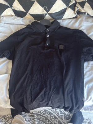 Svart pikétröja med knappdetalj from dolce & Gabbana - Klassisk svart pikétröja med krage och tre knappar framtill. Tröjan har en diskret patch på bröstet och är tillverkad i mjukt material som känns skönt mot huden. Perfekt till jeans eller shorts för en clean look.