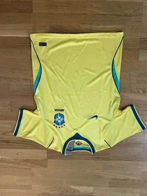Gul Brasilien fotbollströja - Säljer en gul Brasilien fotbollströja från Nike med gröna och blå detaljer. Tröjan har korta ärmar, rund halsringning och det klassiska Brasilien-emblemet på bröstet. Perfekt för fotbollsfans som vill stötta sitt lag.     Fraktar samma eler dagen efter du köpt!!! Endast en kvar i lager!!!