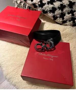 Svart skärp från Salvatore Ferragamo - Snyggt svart skärp från Salvatore Ferragamo med ikoniskt silverfärgat spänne. Skärpet är tillverkat i slätt skinn och har en stilren design som passar till många olika outfits. Levereras med originalförpackning.
