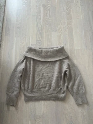 Beige off shoulder stickad tröja - Säljer en beige stickad tröja med bred off shoulder-krage. Tröjan har långa ärmar och ribbade muddar vid ärmslut och nederkant. Perfekt för dig som gillar en avslappnad men ändå trendig stil. Storlek M men sitter bra på en S också! 